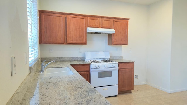 758 Persimmon, Madera, CA 93638 - kitchen featuring white range with gas stovetop, under cabinet range hood, a sink, light stone counters, and brown cabinetry