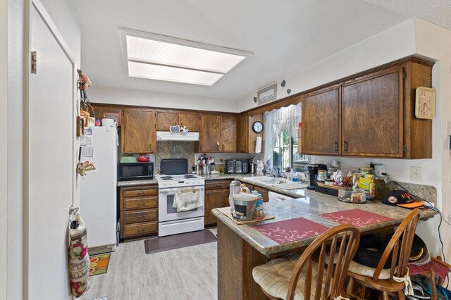 2724 Monocott Dr, Madera, CA 93637 - kitchen with white appliances, a peninsula, under cabinet range hood, light wood-style floors, and a sink