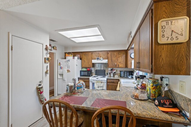 2724 Monocott Dr, Madera, CA 93637 - kitchen featuring white appliances, under cabinet range hood, brown cabinets, a peninsula, and light countertops