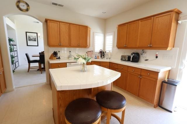 1976 Decatur Ave, Clovis, CA 93611 - kitchen with a kitchen island, arched walkways, brown cabinetry, tasteful backsplash, and light flooring