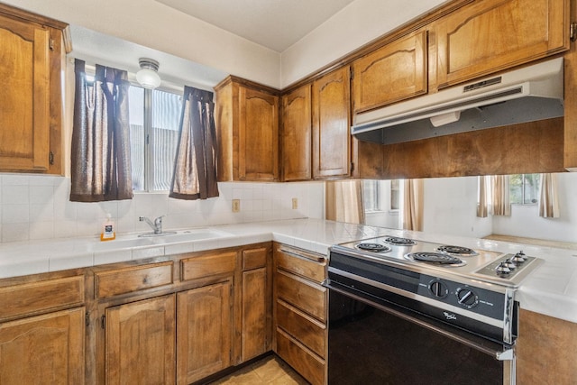 4782 W Austin Way, Fresno, CA 93722 - kitchen with electric range, under cabinet range hood, brown cabinetry, a sink, and decorative backsplash