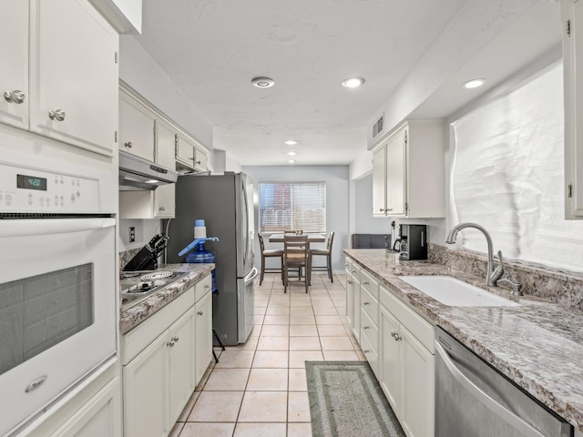 7352 N Adoline Ave, Fresno, CA 93711 - kitchen featuring appliances with stainless steel finishes, a sink, under cabinet range hood, light tile patterned floors, and white cabinetry