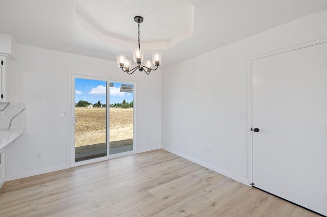 20434 Olympia Rd, Madera, CA 93638 - unfurnished dining area featuring a chandelier, a raised ceiling, light wood finished floors, and baseboards