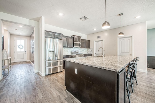 574 Expedition Way, Madera, CA 93636 - kitchen with stainless steel appliances, a sink, a center island with sink, a breakfast bar, and light wood finished floors