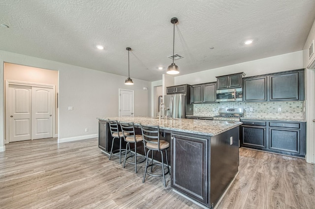 574 Expedition Way, Madera, CA 93636 - kitchen featuring appliances with stainless steel finishes, light wood-style floors, a large island with sink, a breakfast bar, and light stone countertops