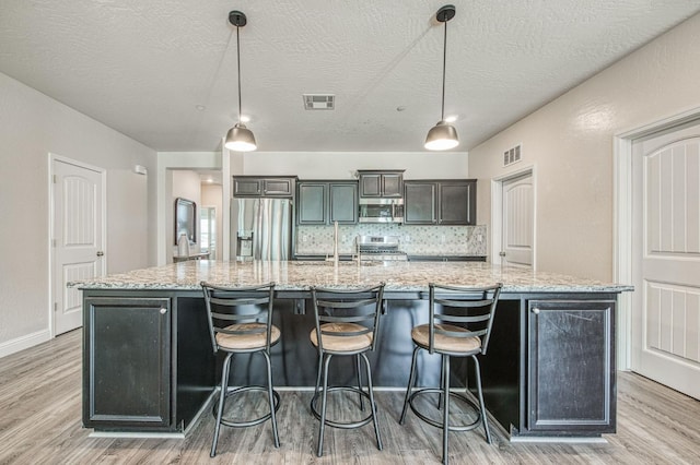 574 Expedition Way, Madera, CA 93636 - kitchen with stainless steel appliances, a large island, light wood-type flooring, a breakfast bar, and a textured ceiling
