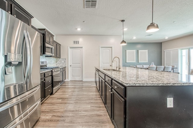 574 Expedition Way, Madera, CA 93636 - kitchen with appliances with stainless steel finishes, a sink, an island with sink, light stone countertops, and light wood-type flooring
