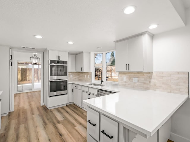 829 Polson Ave, Clovis, CA 93612 - kitchen with double oven, light countertops, a peninsula, light wood-type flooring, and a sink