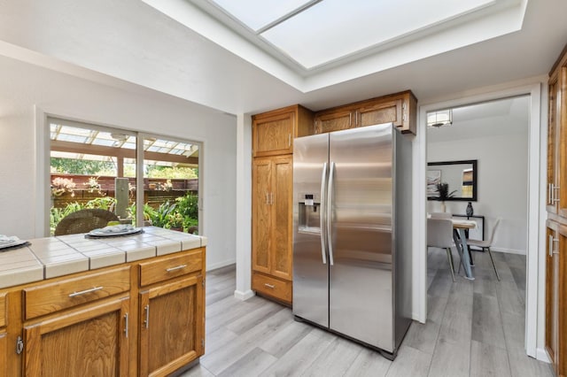 3244 W Fremont Ave, Fresno, CA 93711 - kitchen featuring stainless steel fridge, light wood finished floors, brown cabinetry, tile countertops, and baseboards
