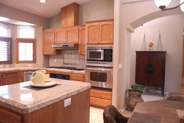 3055 Glenville Ave, Madera, CA 93637 - kitchen with appliances with stainless steel finishes, under cabinet range hood, light tile patterned floors, arched walkways, and tasteful backsplash