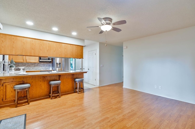 4633 N Glenn Ave, Fresno, CA 93704 - kitchen featuring appliances with stainless steel finishes, a ceiling fan, light wood-type flooring, a peninsula, and a kitchen bar