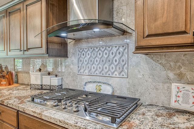 6772 N Wembley Dr, Fresno, CA 93711 - kitchen with wall chimney range hood, stainless steel gas stovetop, decorative backsplash, brown cabinetry, and light stone countertops