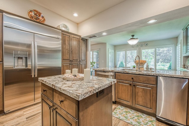 6772 N Wembley Dr, Fresno, CA 93711 - kitchen with appliances with stainless steel finishes, a sink, a kitchen island, light wood finished floors, and light stone counters