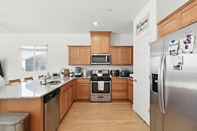 1985 Alma Ct, Chowchilla, CA 93610 - kitchen with appliances with stainless steel finishes, a peninsula, light wood-type flooring, light stone countertops, and a sink