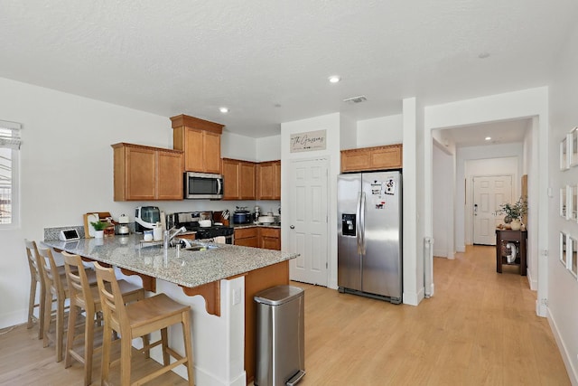 1985 Alma Ct, Chowchilla, CA 93610 - kitchen featuring appliances with stainless steel finishes, a peninsula, light wood-style flooring, brown cabinets, and a kitchen breakfast bar