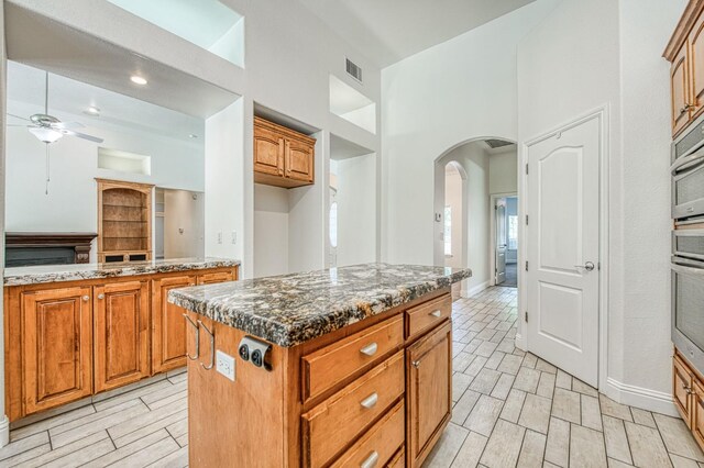 1251 E Rosemont Ln, Fresno, CA 93730 - kitchen featuring arched walkways, a ceiling fan, brown cabinetry, dark stone counters, and a center island