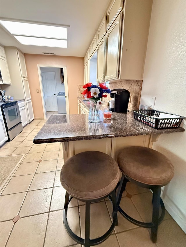 31117 Longview Ln E, Coarsegold, CA 93614 - kitchen featuring electric stove, washer / dryer, decorative backsplash, a peninsula, and a breakfast bar area