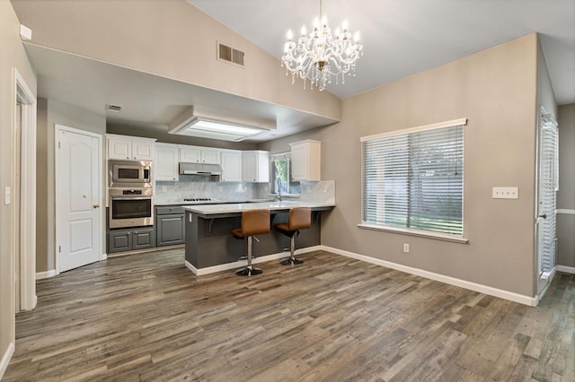10131 N Price Ave, Fresno, CA 93730 - kitchen with stainless steel appliances, under cabinet range hood, dark wood-style flooring, white cabinetry, and decorative backsplash