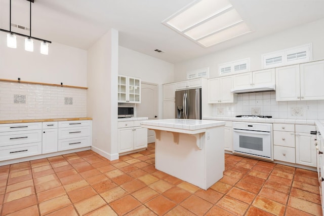 2189 W Via Delfini, Fresno, CA 93711 - kitchen with appliances with stainless steel finishes, tile countertops, decorative backsplash, white cabinets, and a center island