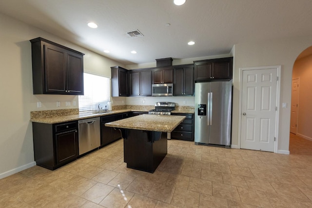 3083 N Stanley Ave, Fresno, CA 93737 - kitchen featuring stainless steel appliances, arched walkways, a sink, a kitchen island, and baseboards