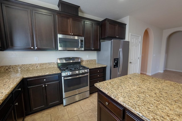 3083 N Stanley Ave, Fresno, CA 93737 - kitchen featuring appliances with stainless steel finishes, light tile patterned flooring, dark brown cabinetry, and light stone counters
