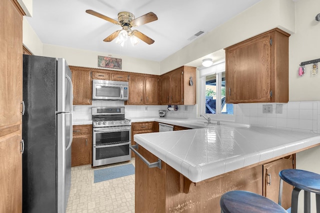 5072 N Forkner Ave, Fresno, CA 93711 - kitchen featuring appliances with stainless steel finishes, a peninsula, a sink, a ceiling fan, and tasteful backsplash