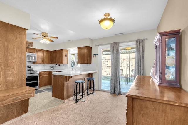 5072 N Forkner Ave, Fresno, CA 93711 - kitchen with stainless steel appliances, a kitchen bar, brown cabinetry, a ceiling fan, and a peninsula