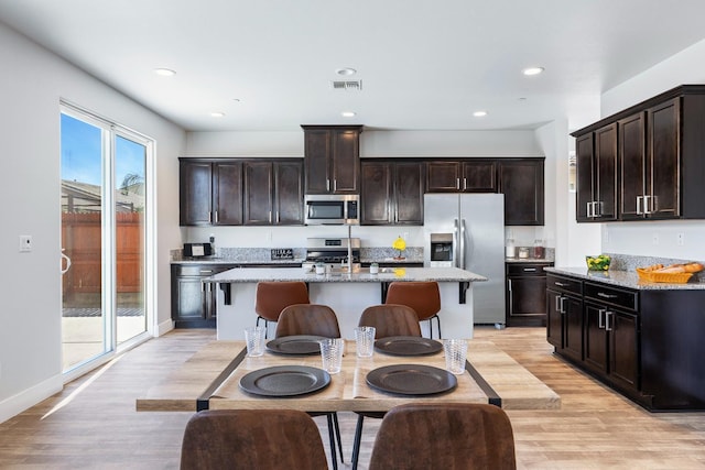 1276 Sauret St, Madera, CA 93638 - kitchen with appliances with stainless steel finishes, light wood-style flooring, an island with sink, light stone counters, and recessed lighting