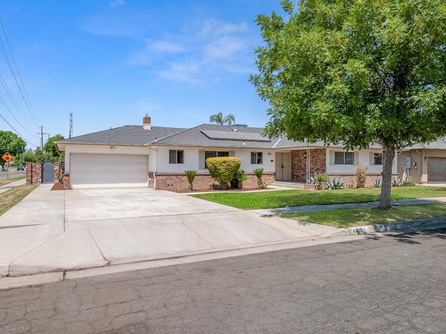 6413 N 5th St, Fresno, CA 93710 - ranch-style house with brick siding, solar panels, an attached garage, a front lawn, and driveway