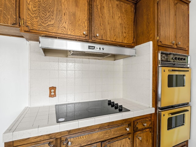 6413 N 5th St, Fresno, CA 93710 - kitchen featuring under cabinet range hood, double wall oven, black electric stovetop, decorative backsplash, and brown cabinets