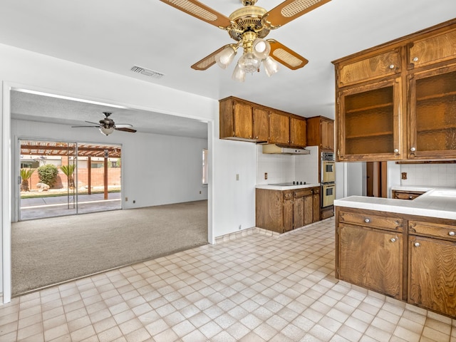 6413 N 5th St, Fresno, CA 93710 - kitchen with ceiling fan, light colored carpet, under cabinet range hood, brown cabinetry, and light countertops