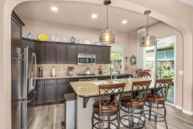 3675 Trenton Ln, Clovis, CA 93619 - kitchen with stainless steel appliances, light wood-style floors, dark brown cabinets, decorative backsplash, and light stone counters