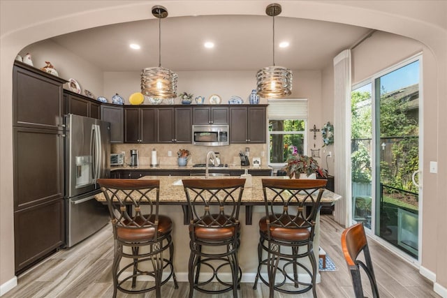 3675 Trenton Ln, Clovis, CA 93619 - kitchen featuring appliances with stainless steel finishes, dark brown cabinets, light wood finished floors, backsplash, and a breakfast bar area