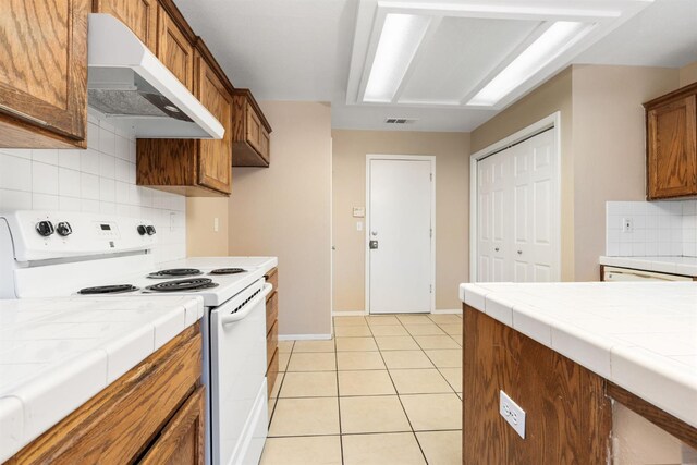 6051 N Tracy Ave, Fresno, CA 93722 - kitchen featuring electric range, under cabinet range hood, tile counters, decorative backsplash, and brown cabinets