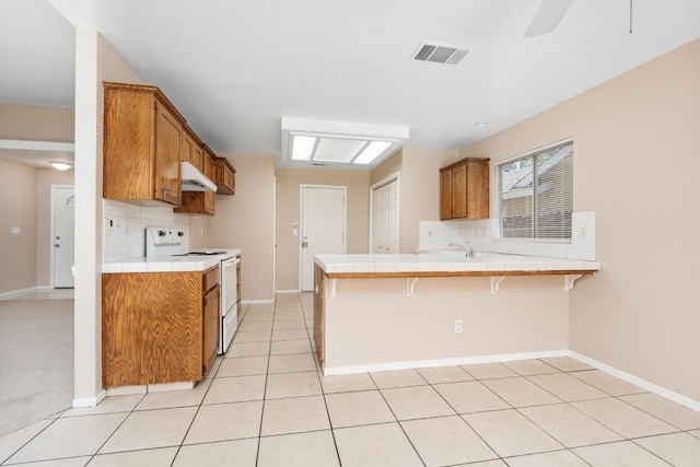 6051 N Tracy Ave, Fresno, CA 93722 - kitchen with white range with electric stovetop, tile counters, under cabinet range hood, and brown cabinetry