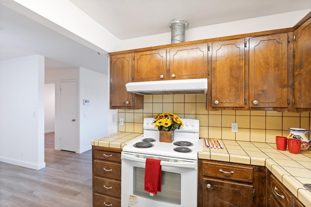 4003 E El Monte Way, Fresno, CA 93702 - kitchen featuring white electric stove, under cabinet range hood, tile counters, tasteful backsplash, and light wood-style floors