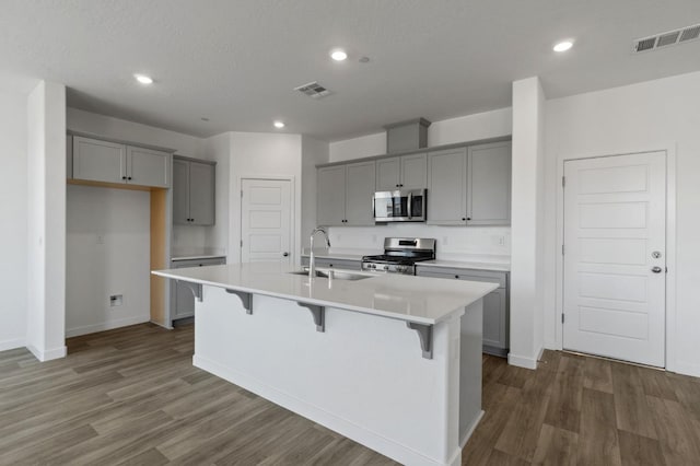 3210 Frontera Ave, Clovis, CA 93619 - kitchen with stainless steel appliances, gray cabinets, a sink, dark wood-type flooring, and a center island with sink