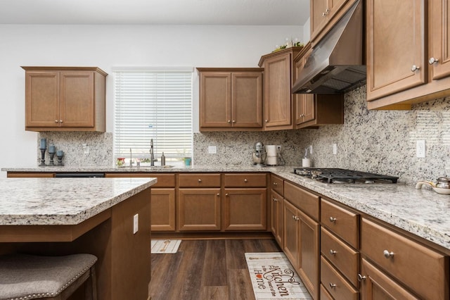 2027 N Bliss Ave, Fresno, CA 93727 - kitchen featuring under cabinet range hood, stainless steel gas cooktop, dark wood finished floors, decorative backsplash, and brown cabinetry