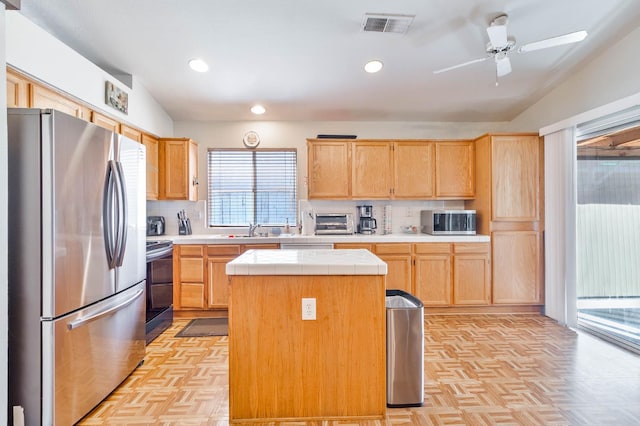 5572 W Indianapolis Ave, Fresno, CA 93722 - kitchen with appliances with stainless steel finishes, light brown cabinets, tile countertops, a center island, and tasteful backsplash
