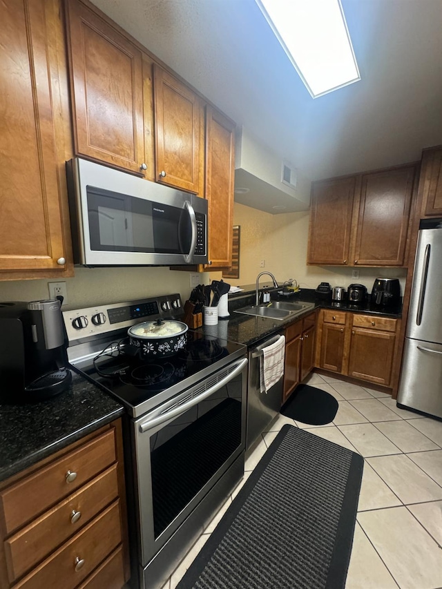 7166 N Fruit Ave Unit 160, Fresno, CA 93711 - kitchen with stainless steel appliances, a sink, light tile patterned flooring, brown cabinetry, and dark stone counters