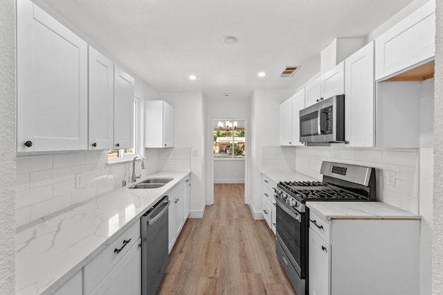2543 E Ashcroft Ave, Fresno, CA 93726 - kitchen with appliances with stainless steel finishes, a sink, light wood-style floors, light stone countertops, and white cabinetry