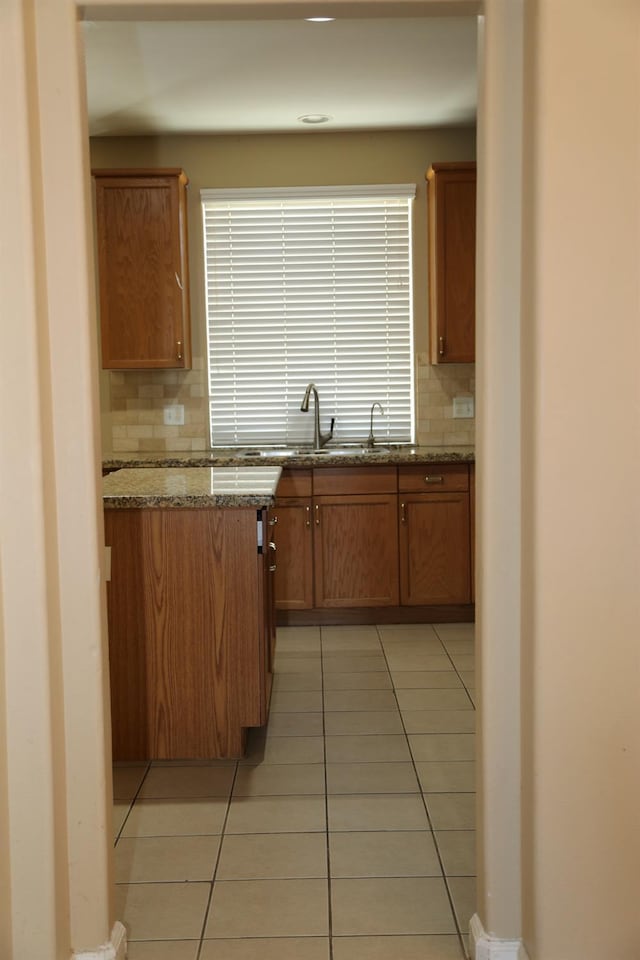 5811 W Cromwell Ave, Fresno, CA 93722 - kitchen with backsplash, light tile patterned floors, a sink, and brown cabinets
