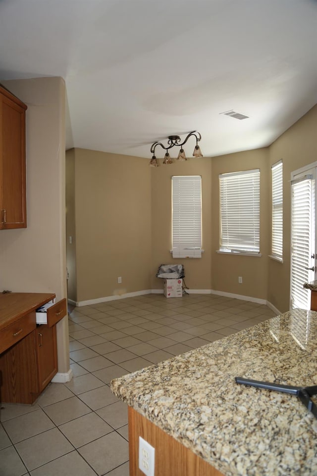 5811 W Cromwell Ave, Fresno, CA 93722 - kitchen featuring light tile patterned floors, brown cabinetry, light stone counters, and baseboards