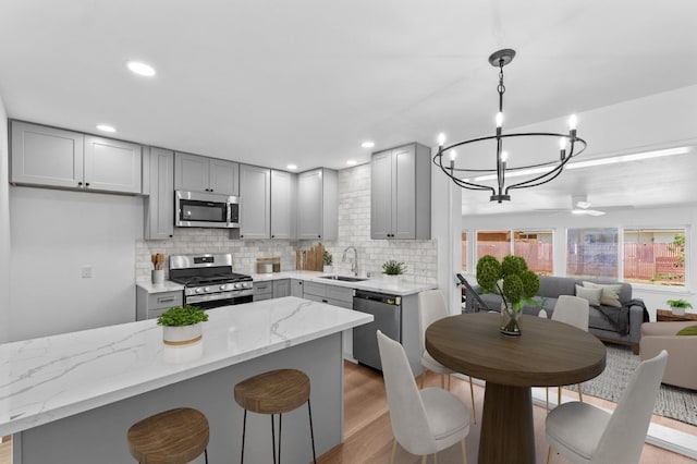3926 N Kavanagh Ave, Fresno, CA 93705 - kitchen with stainless steel appliances, gray cabinetry, a sink, decorative backsplash, and light stone counters