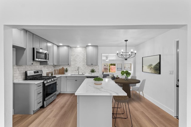 3926 N Kavanagh Ave, Fresno, CA 93705 - kitchen with appliances with stainless steel finishes, gray cabinetry, a sink, a kitchen bar, and light wood-style flooring