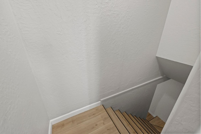 staircase with wood finished floors, a textured wall, and baseboards
