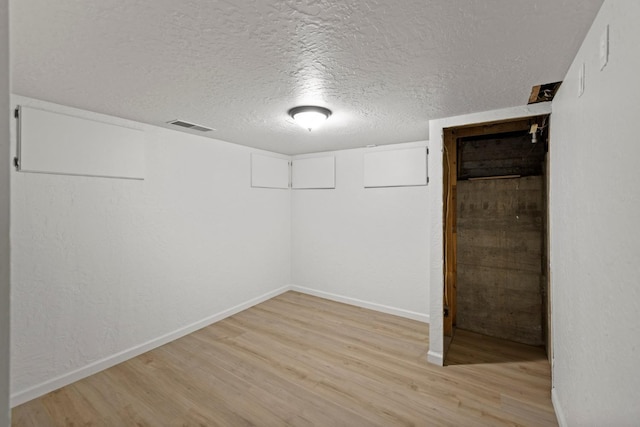 finished basement with light wood-style floors, baseboards, and a textured ceiling