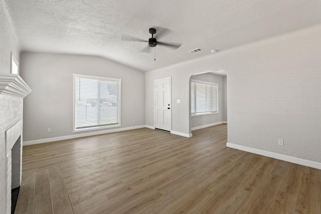 unfurnished living room featuring a ceiling fan, a brick fireplace, arched walkways, wood finished floors, and lofted ceiling