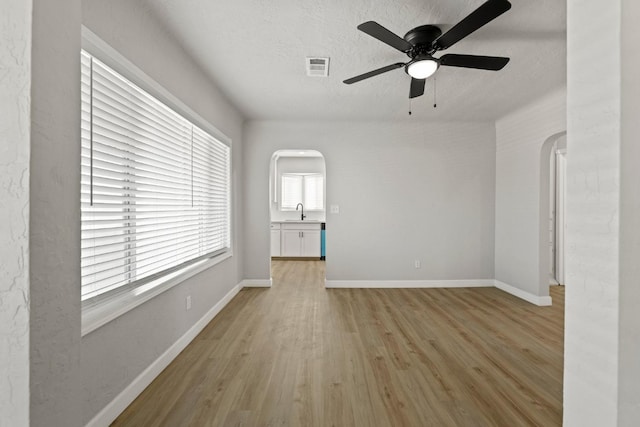 unfurnished living room featuring arched walkways, light wood-style floors, a sink, ceiling fan, and baseboards