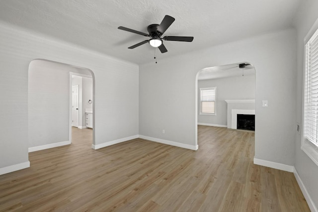 unfurnished living room featuring arched walkways, a ceiling fan, light wood-style flooring, a fireplace, and baseboards